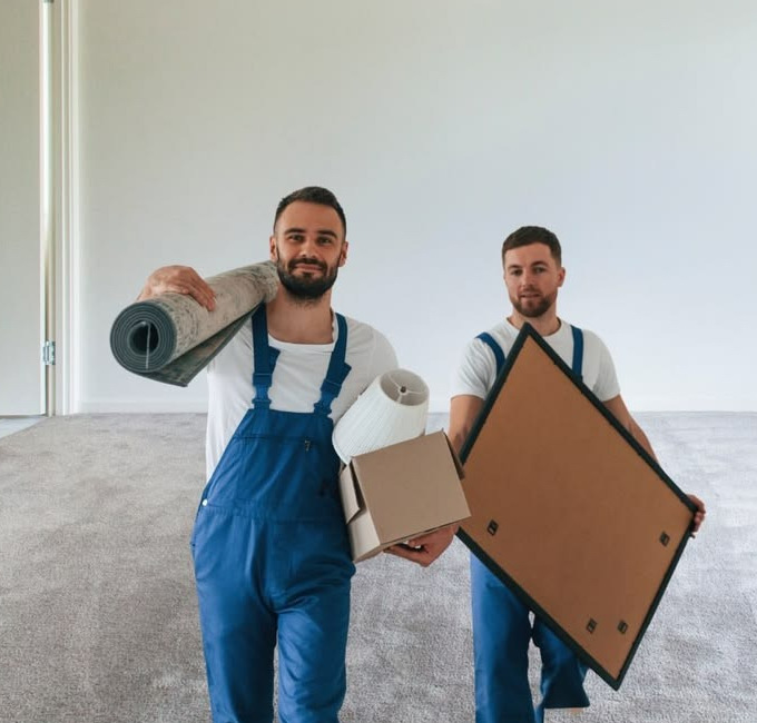 Twee professionele ontruimers van Omegaservice dragen tapijt, dozen en een schilderij uit een lege woning